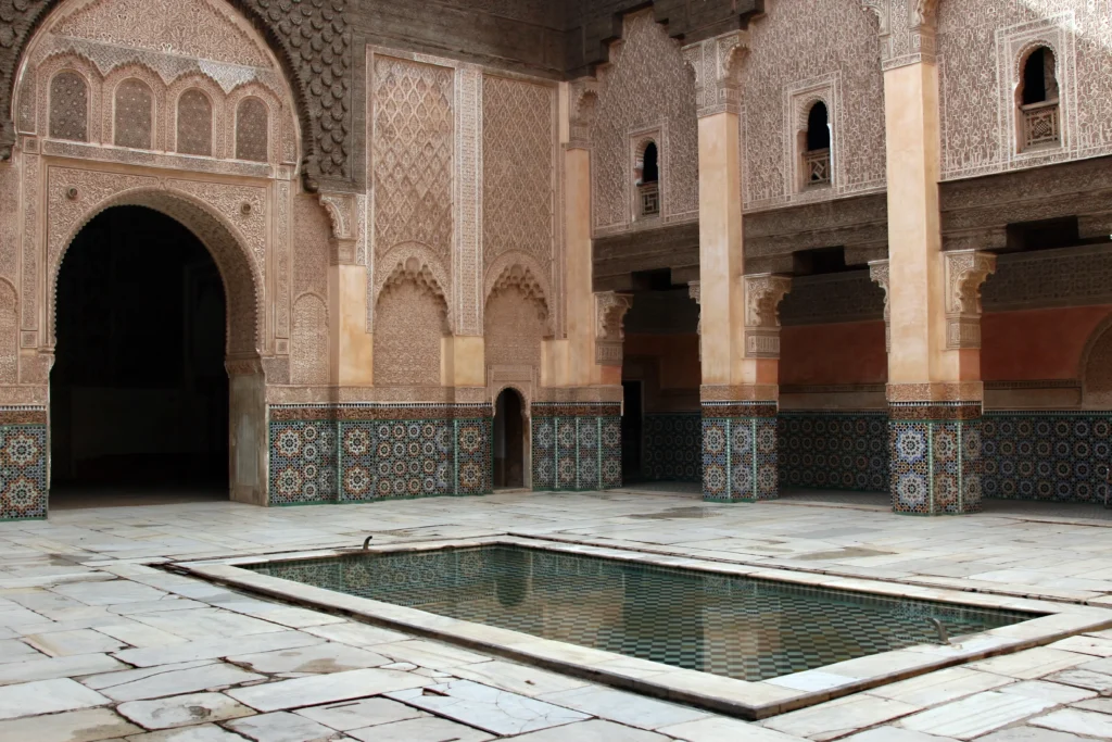 Where to stay in Marrakech: traditional Moroccan courtyard with intricate mosaic tiles, carved arches, and a central reflecting pool.